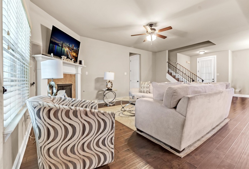 Living area with stairway, ceiling fan, dark wood-type flooring, and a tiled fireplace