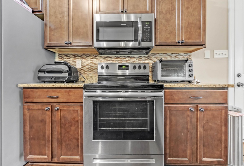 Kitchen with light stone countertops, stainless steel appliances, backsplash, and brown cabinets