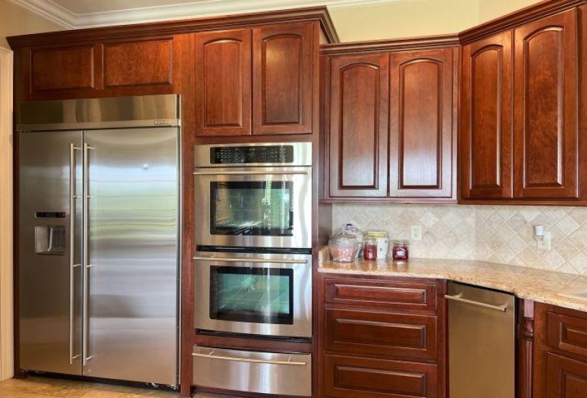 Kitchen featuring light stone counters, crown molding, decorative backsplash, a warming drawer, and appliances with stainless steel finishes