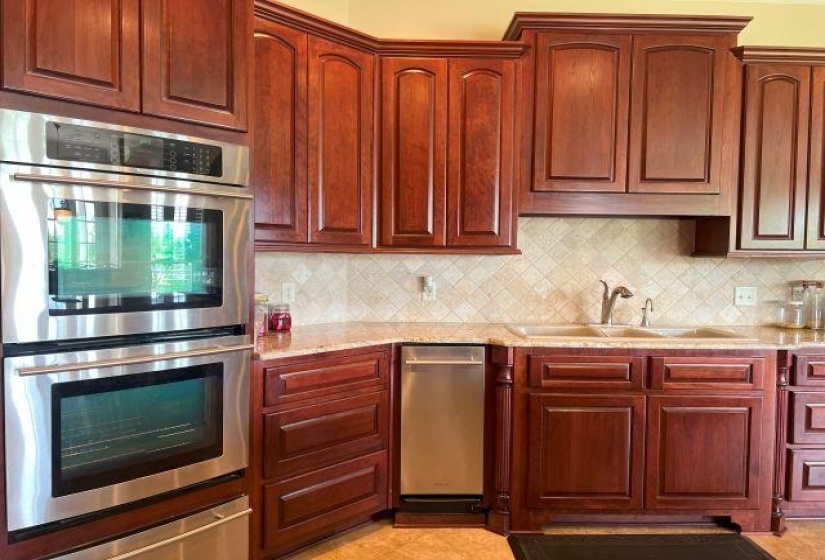 Kitchen featuring a sink, backsplash, stainless steel double oven, light stone countertops, and a warming drawer