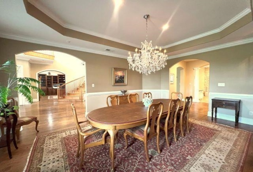Dining area featuring wainscoting, a chandelier, wood finished floors, arched walkways, and a raised ceiling