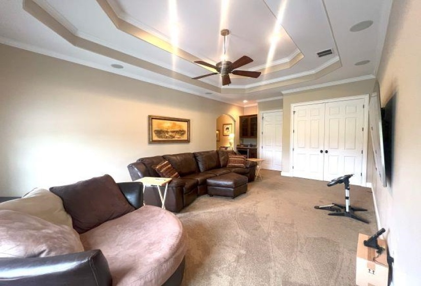 Living area featuring a tray ceiling, ornamental molding, ceiling fan, arched walkways, and carpet floors