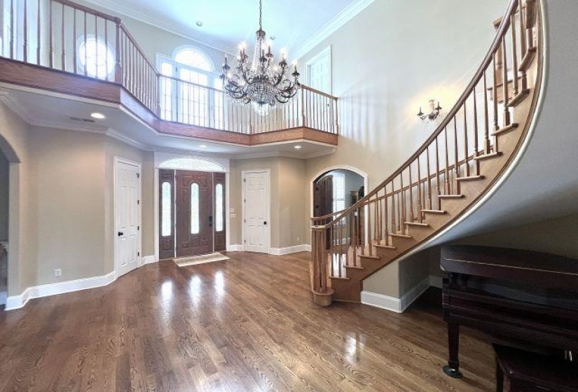 Entrance foyer with arched walkways, ornamental molding, a towering ceiling, wood finished floors, and a chandelier