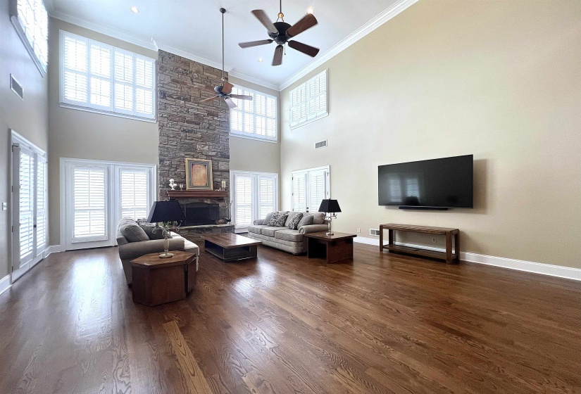 Living room featuring dark wood finished floors, ornamental molding, a stone fireplace, ceiling fan, and a towering ceiling