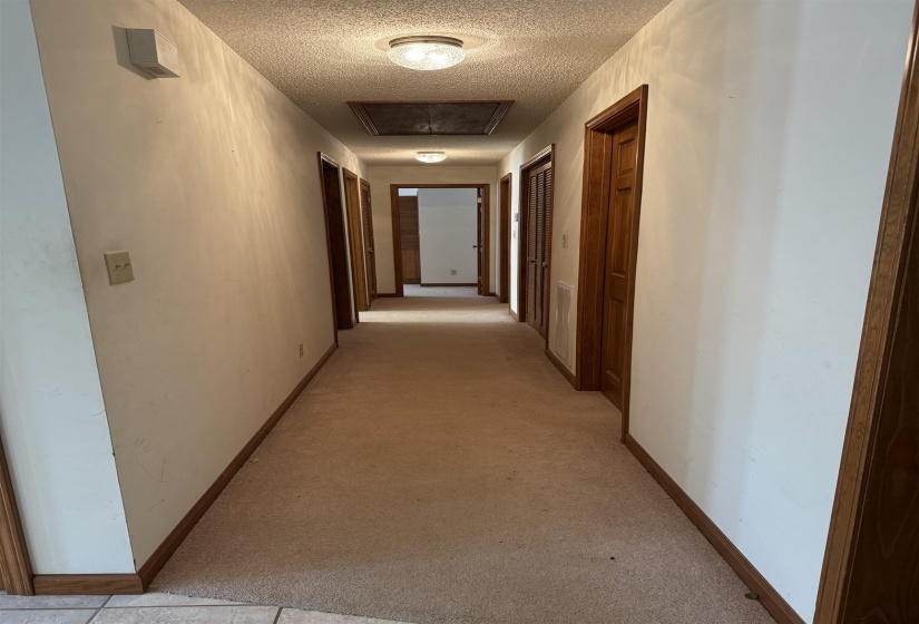 Hall featuring baseboards, light carpet, and a textured ceiling