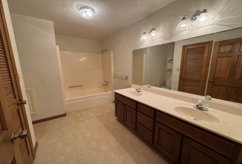 Full bath with double vanity, bathtub / shower combination, a sink, tile patterned floors, and a textured ceiling