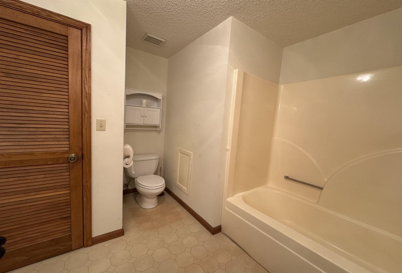 Full bathroom featuring toilet, a textured ceiling, baseboards, and visible vents