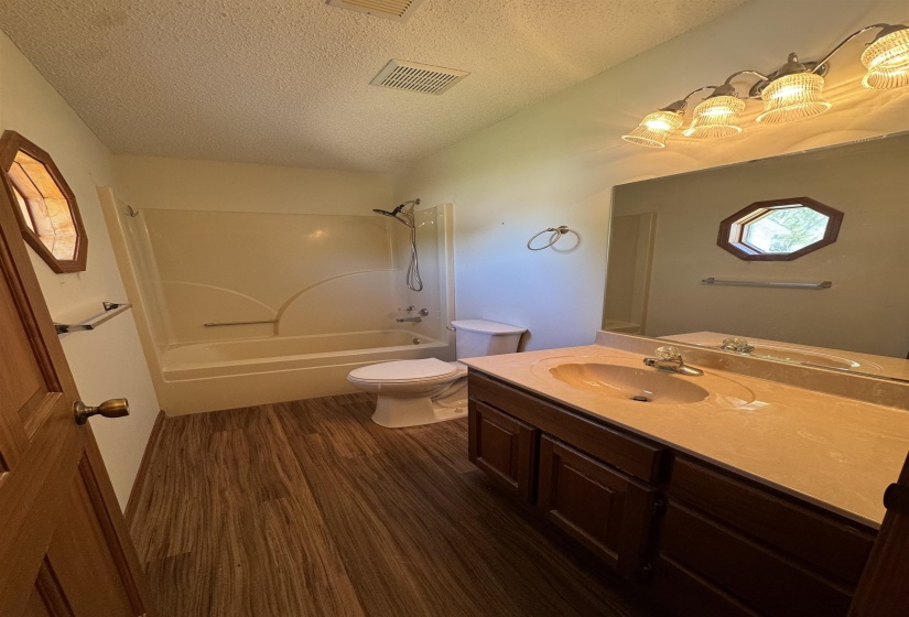 Full bath featuring toilet, tub / shower combination, wood finished floors, a textured ceiling, and visible vents
