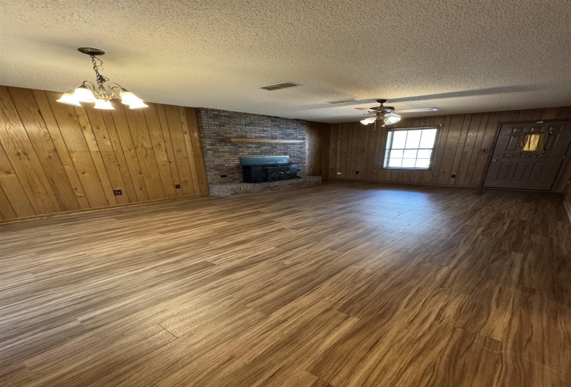 Unfurnished living room featuring wood finished floors, a fireplace, a textured ceiling, wood walls, and visible vents