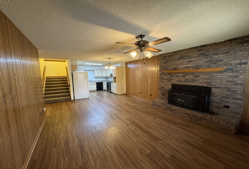 Unfurnished living room with a fireplace, dark wood-style flooring, wooden walls, and ceiling fan