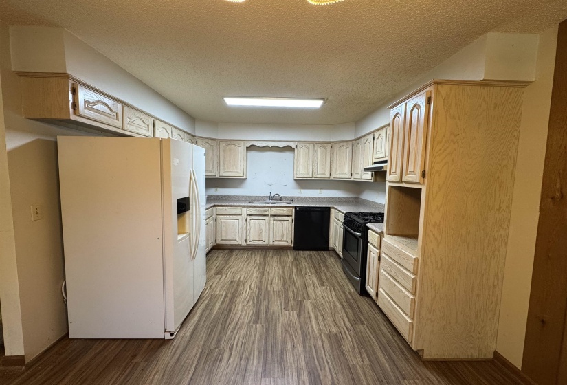 Kitchen with a sink, stainless steel gas range oven, a textured ceiling, white fridge with ice dispenser, and dishwasher