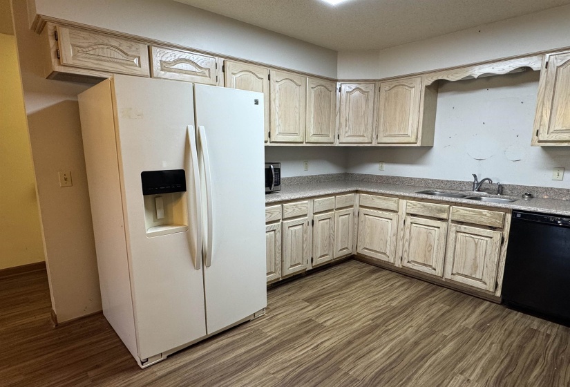 Kitchen featuring light countertops, a sink, white refrigerator with ice dispenser, dishwasher, and dark wood-style floors