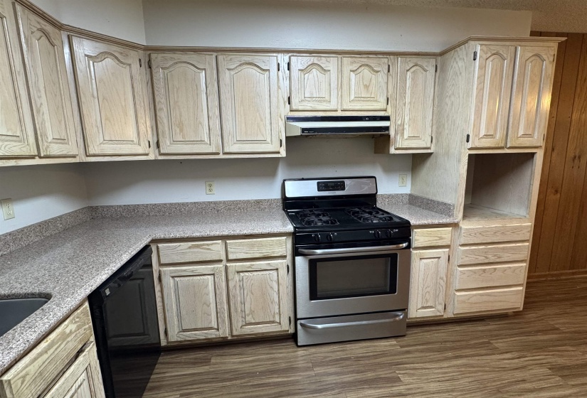 Kitchen with stainless steel gas range, light countertops, under cabinet range hood, and dishwasher