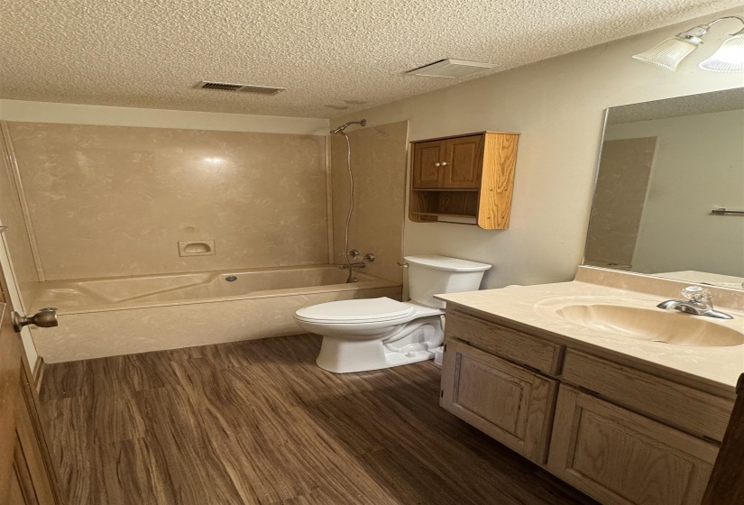 Full bathroom featuring toilet, wood finished floors, a textured ceiling, visible vents, and tub / shower combination