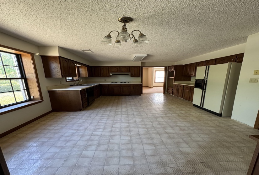 Kitchen with light countertops, a chandelier, white fridge with ice dispenser, and a healthy amount of sunlight