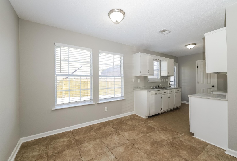 Kitchen with tasteful backsplash, white dishwasher, tile floors, sink, and white cabinetry