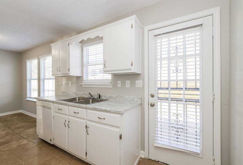 Kitchen featuring white dishwasher, sink, tile floors, and white cabinetry