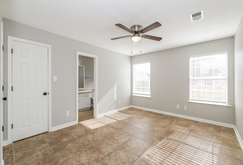 Unfurnished bedroom with ensuite bath, ceiling fan, and light tile floors
