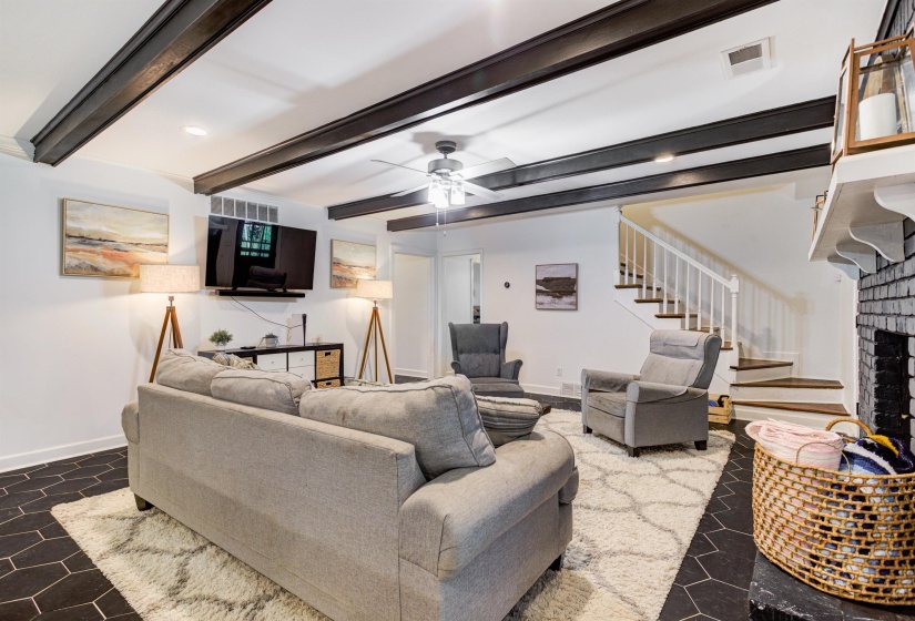 Living room featuring stairway, baseboards, a ceiling fan, a fireplace, and beamed ceiling