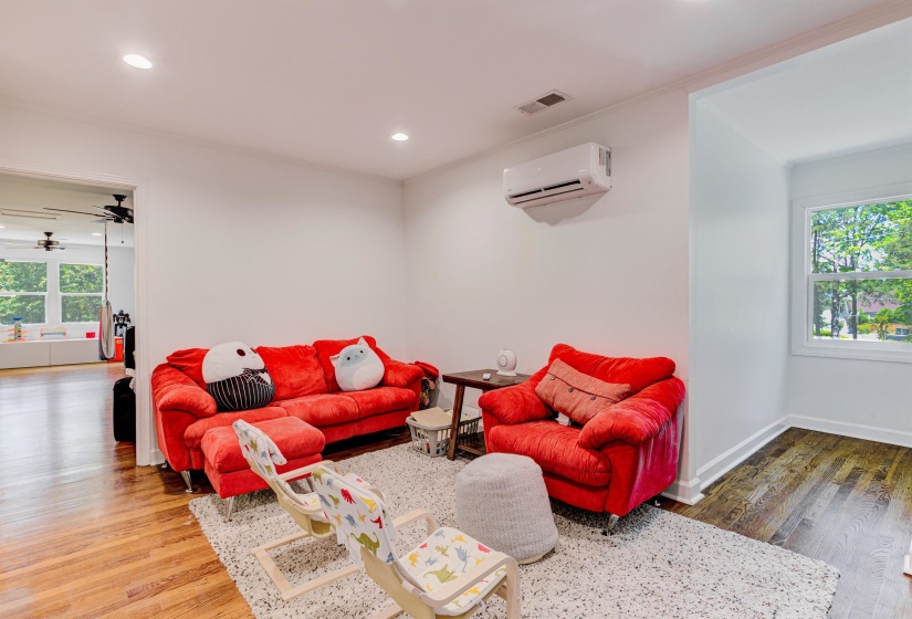 Living room with a wall mounted air conditioner, wood finished floors, recessed lighting, and baseboards