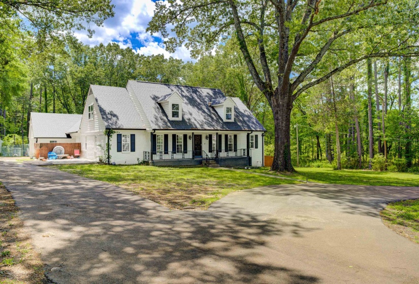 Cape cod home with covered porch, a front lawn, and view of scattered trees