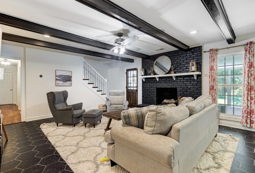 Living room featuring stairs, beamed ceiling, plenty of natural light, a fireplace, and ceiling fan