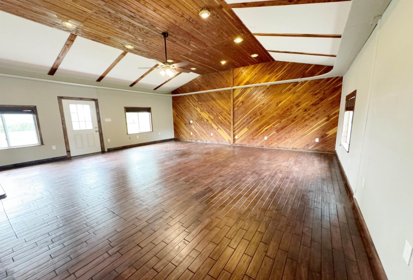 Unfurnished living room with wooden walls, dark wood finished floors, lofted ceiling, a ceiling fan, and baseboards