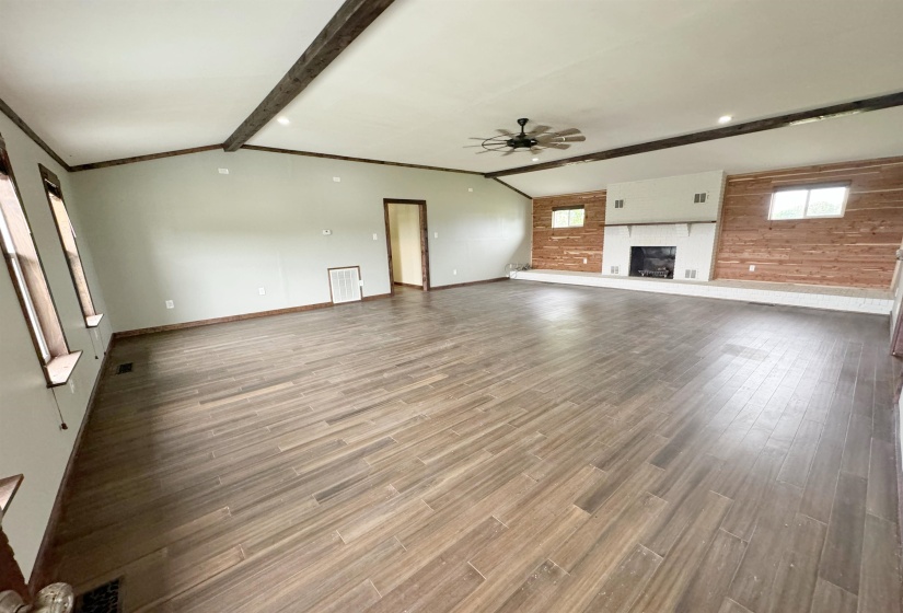 Unfurnished living room with ceiling fan, a large fireplace, baseboards, and wood finished floors