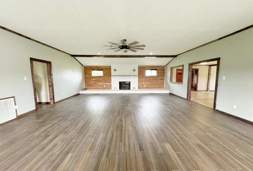 Unfurnished living room featuring ceiling fan, baseboards, crown molding, wood finished floors, and a fireplace with raised hearth