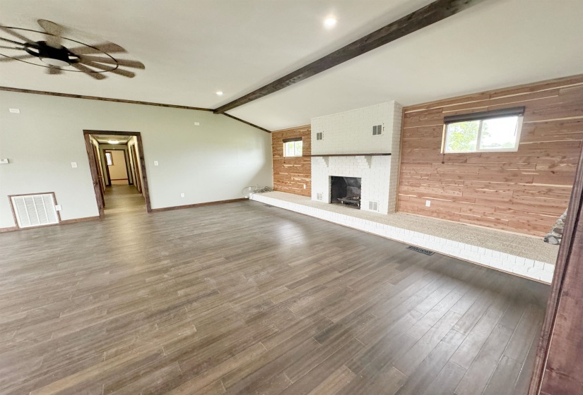 Unfurnished living room with wooden walls, a brick fireplace, wood finished floors, baseboards, and ceiling fan