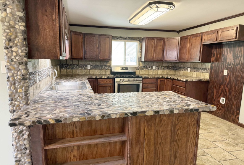 Kitchen with gas stove, a sink, a peninsula, decorative backsplash, and ornamental molding