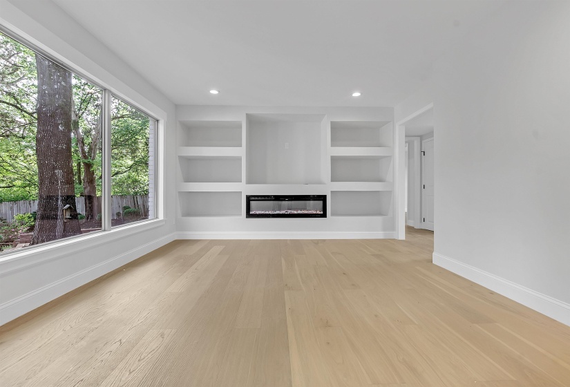 Unfurnished living room with baseboards, light wood finished floors, built in features, a glass covered fireplace, and recessed lighting