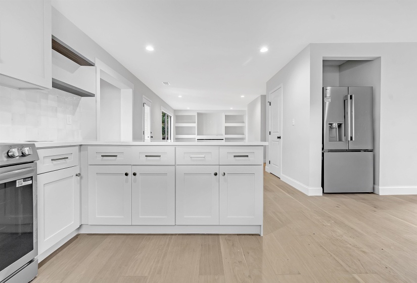 Kitchen with stainless steel refrigerator with ice dispenser, open shelves, range, a peninsula, and light countertops