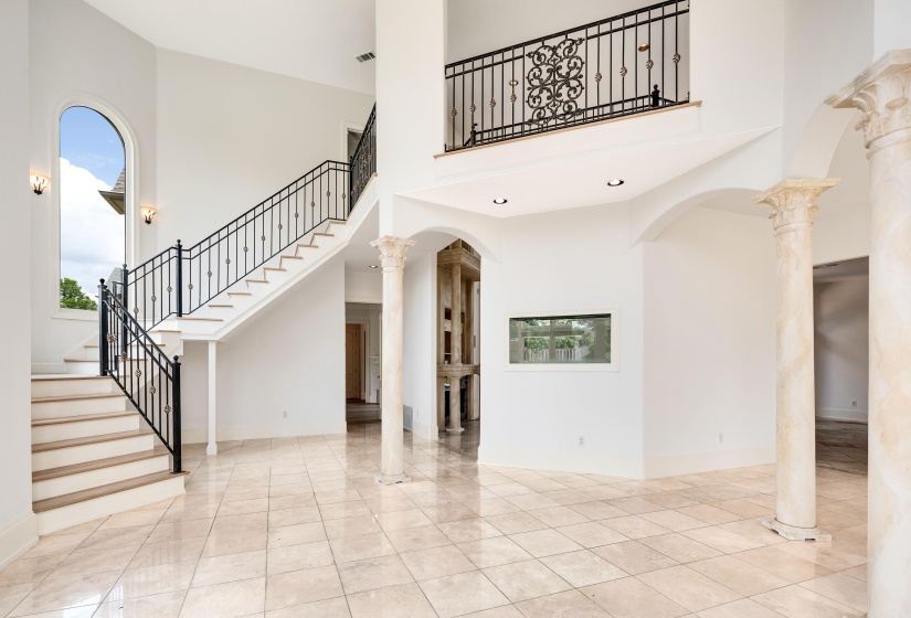 Unfurnished living room with a towering ceiling, stairway, baseboards, and ornate columns