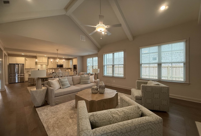 Living room featuring high vaulted ceiling, beamed ceiling, a ceiling fan, a chandelier, and dark wood-type flooring