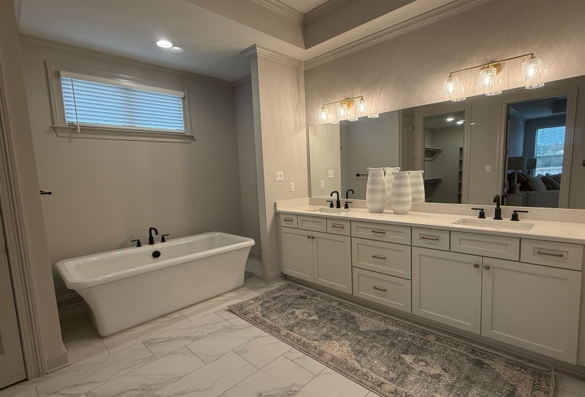 Bathroom with double vanity, a freestanding tub, crown molding, light marble finish flooring, and recessed lighting