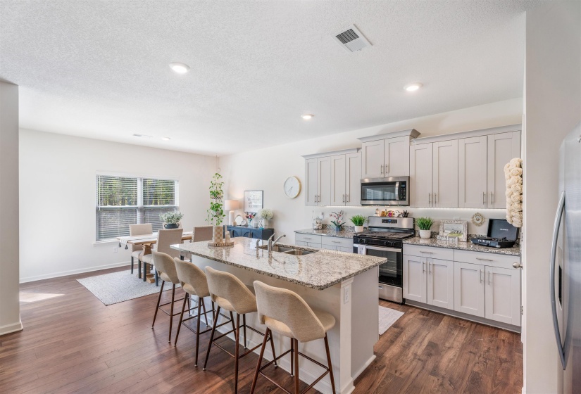 Kitchen with stainless steel appliances, a sink, a breakfast bar, an island with sink, and dark wood-type flooring