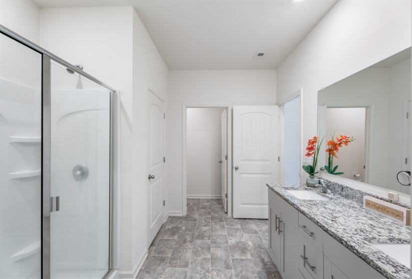 Bathroom with a shower stall, double vanity, stone finish floors, and baseboards