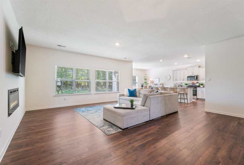 Living area with dark wood-style floors, a glass covered fireplace, baseboards, recessed lighting, and a textured ceiling