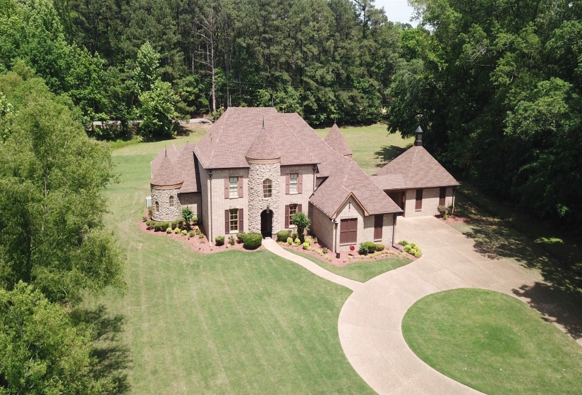 French country home featuring stone siding, a front yard, a shingled roof, a forest view, and driveway