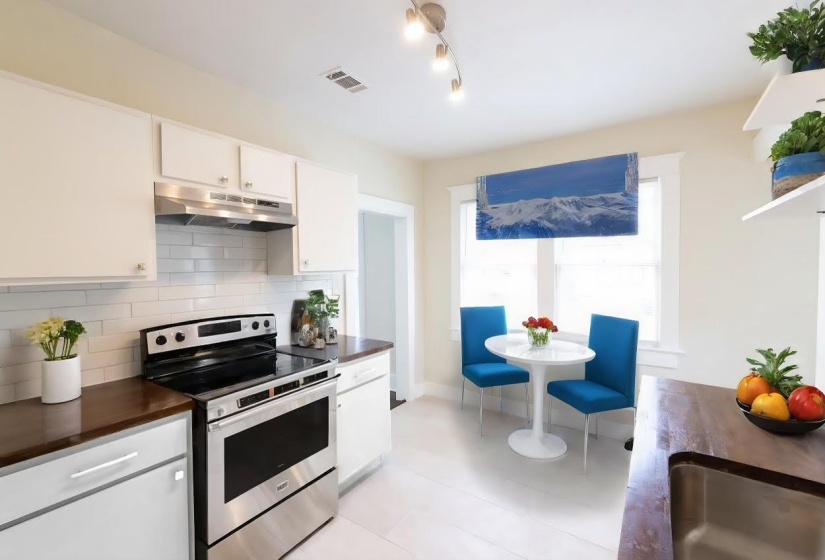 Kitchen featuring decorative backsplash, stainless steel electric stove, sink, light tile patterned floors, and white cabinets