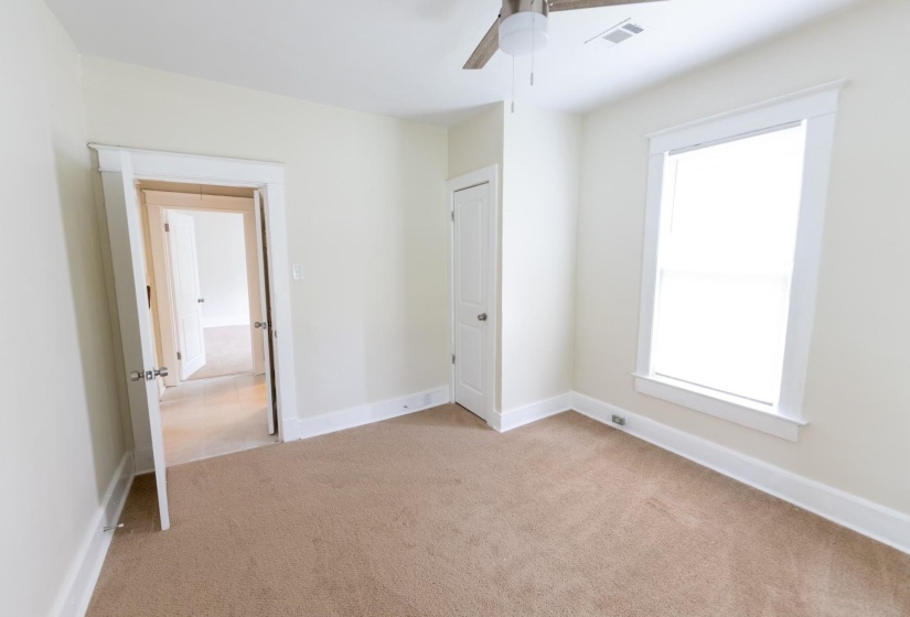 Unfurnished bedroom with ceiling fan, light carpet, and multiple windows