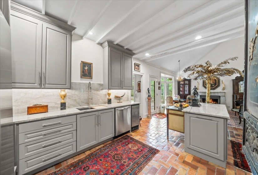 Kitchen with gray cabinetry, a sink, stainless steel dishwasher, backsplash, and a warm lit fireplace
