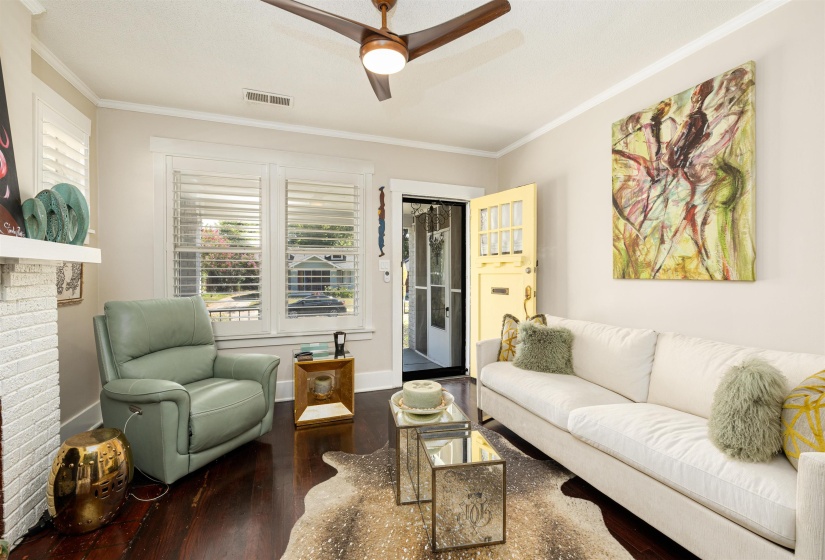 Living area with wood finished floors, crown molding, ceiling fan, baseboards, and a brick fireplace