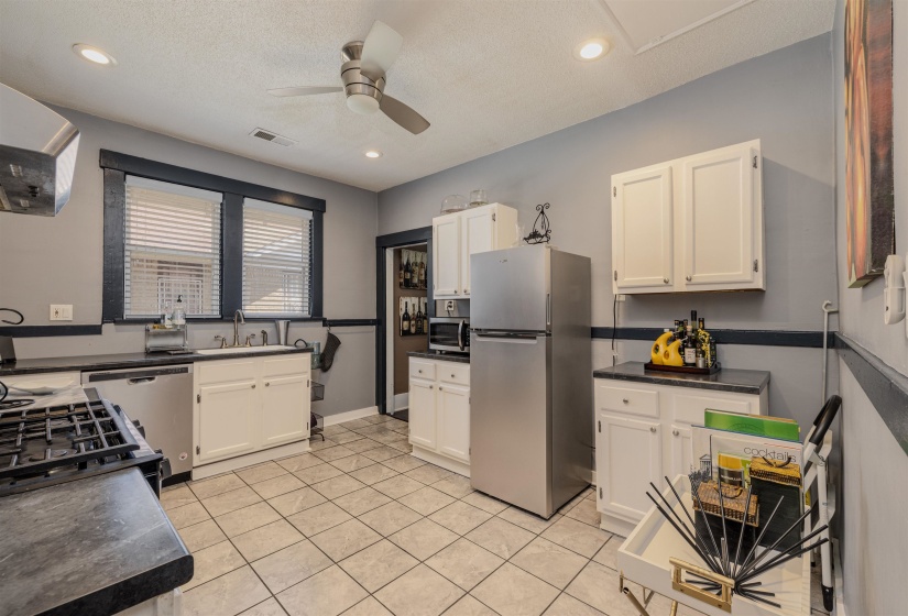 Kitchen with appliances with stainless steel finishes, dark countertops, white cabinetry, ceiling fan, and a sink