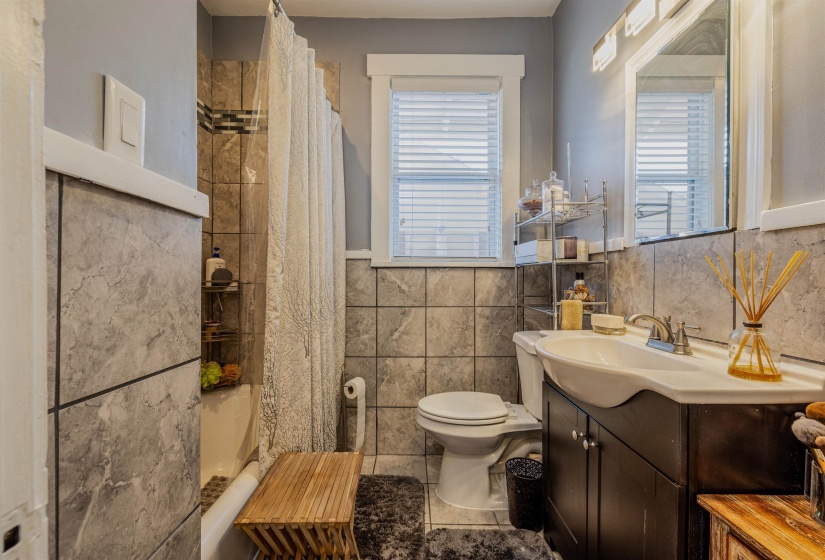 Full bath with tile walls, toilet, a shower with shower curtain, vanity, and a wainscoted wall