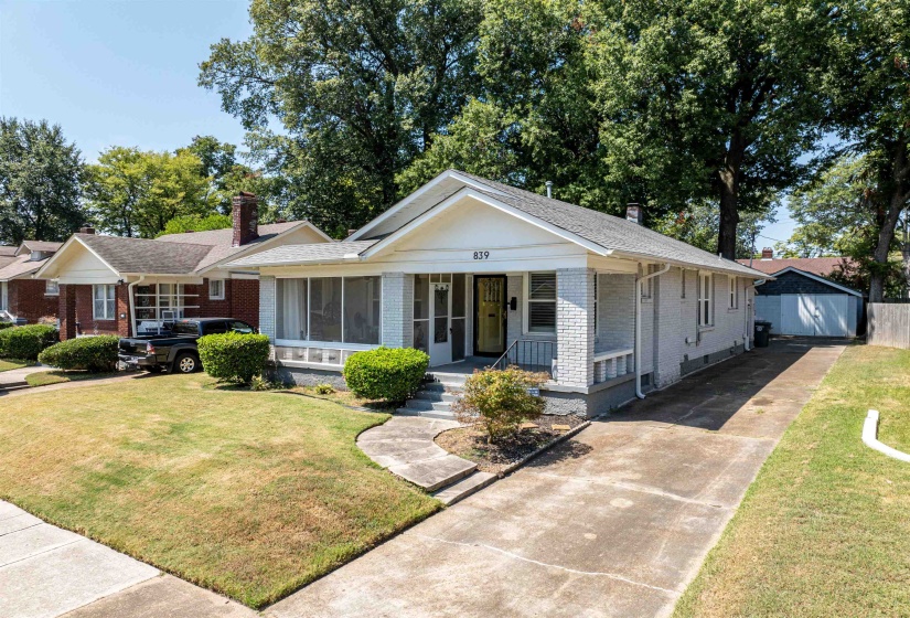 View of front of home with concrete driveway, brick siding, a porch, a front lawn, and a chimney