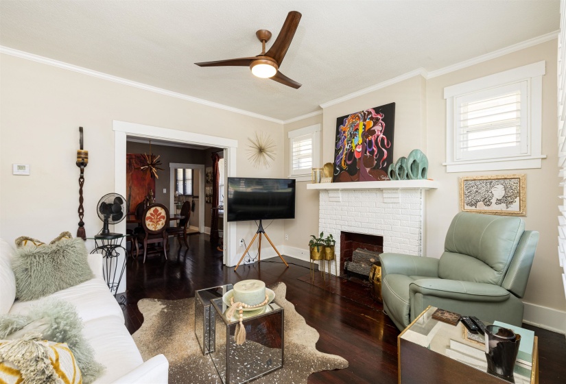 Living room featuring wood finished floors, ceiling fan, ornamental molding, baseboards, and a fireplace