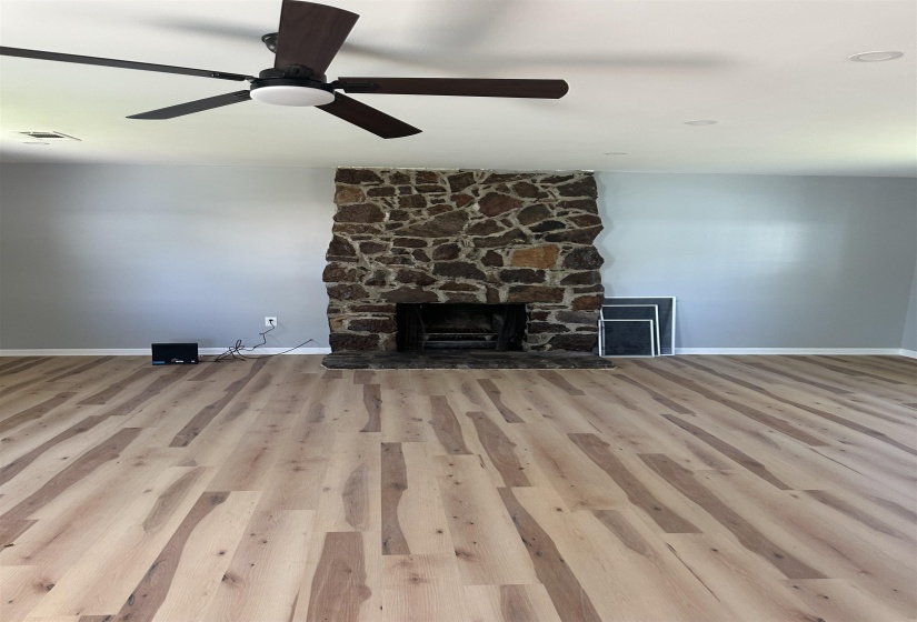 Unfurnished living room with a ceiling fan, a stone fireplace, baseboards, and wood finished floors