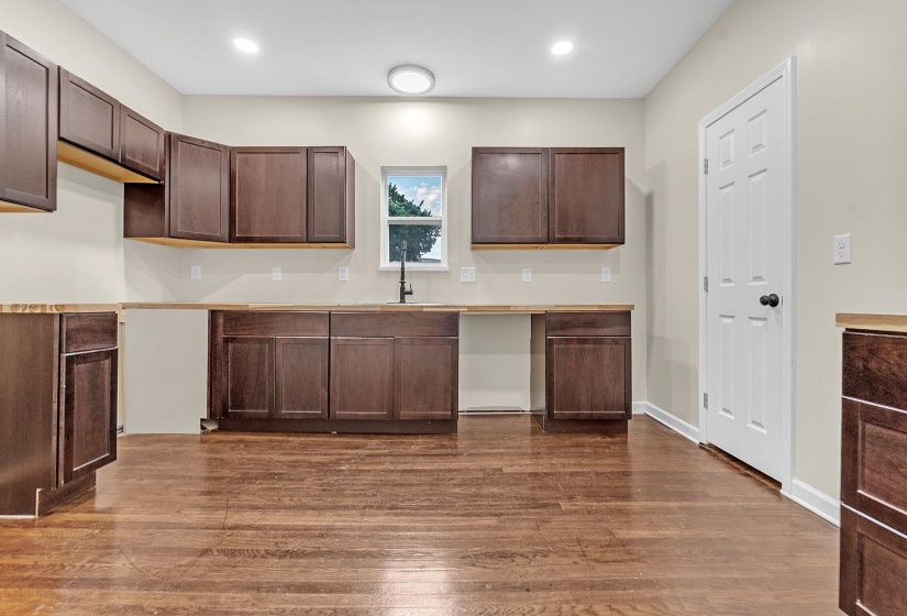 Kitchen with a sink, dark brown cabinetry, dark wood-type flooring, recessed lighting, and light countertops